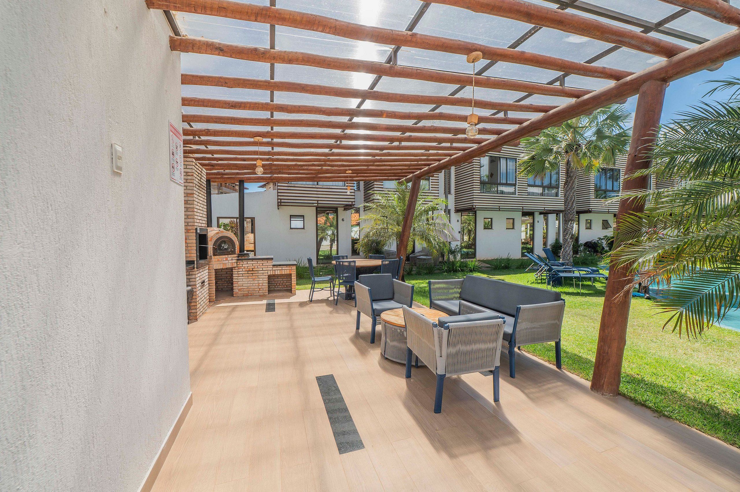 Een buitenpatio met een houten pergola, een bakstenen barbecue en tuinmeubilair.