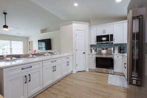 Una cocina moderna con armarios blancos, electrodomésticos de acero inoxidable y una isla grande con microondas integrado.