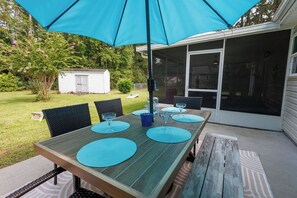 An outdoor dining area with a table set for four, a blue umbrella, and a covered patio.