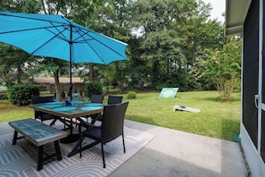 Un patio al aire libre con una mesa, sillas, un paraguas azul y un césped.