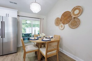 A modern kitchen with a stainless steel refrigerator, a dining table set with plates and napkins, and a view of a balcony with outdoor furniture.