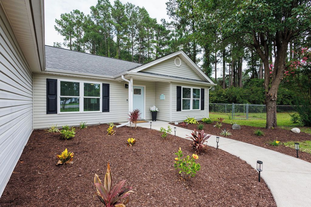 A single-story house with a front porch, a landscaped garden with various plants, and a pathway leading to the entrance.