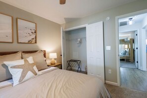 A bedroom with a bed, bedside lamps, a closet, and a hallway leading to another room.