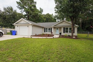A single-story house with a garage, a front yard with a small garden, and a tree in front of the house.