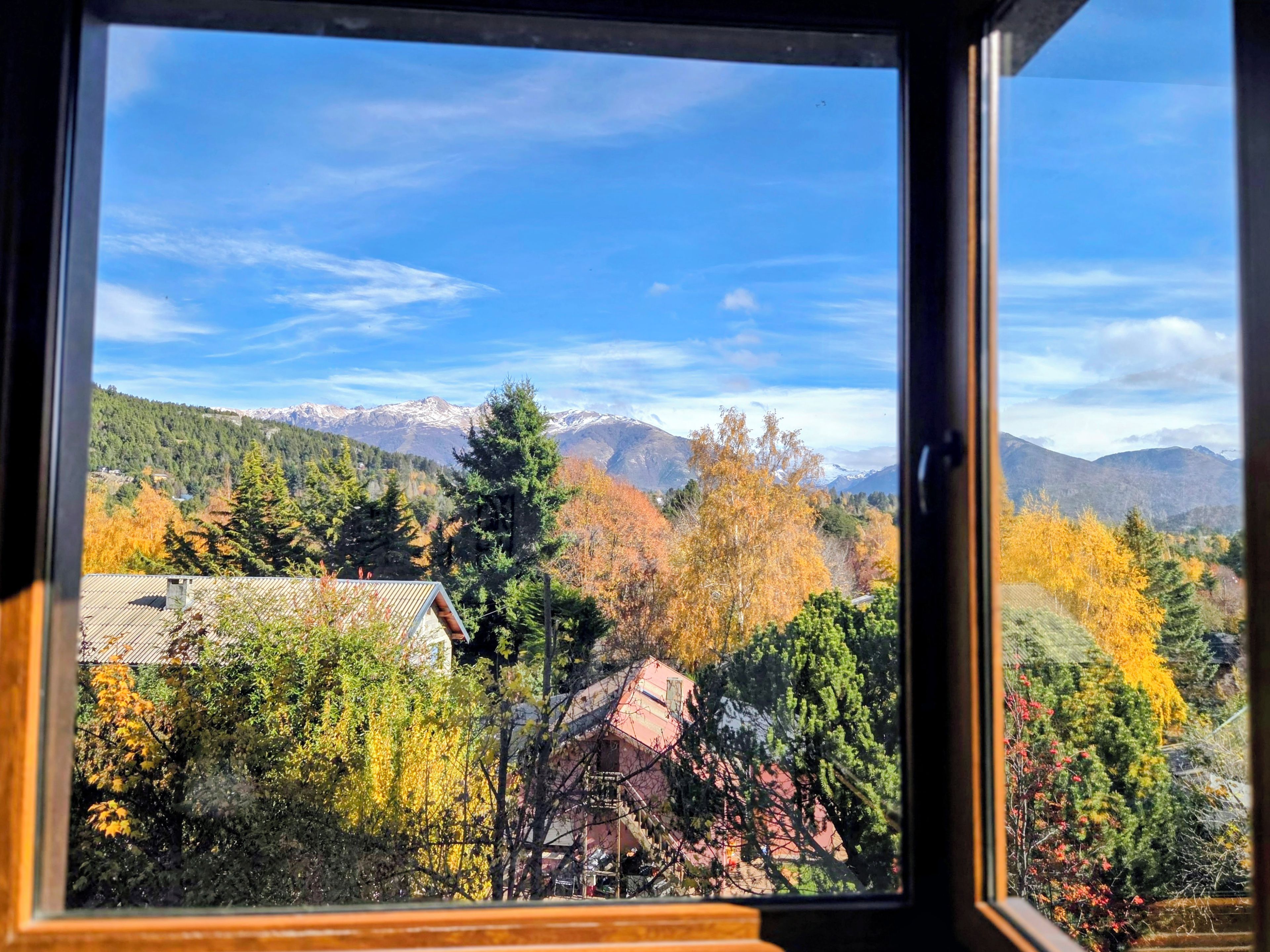 A view through a window with a mountain landscape, including trees and a building.