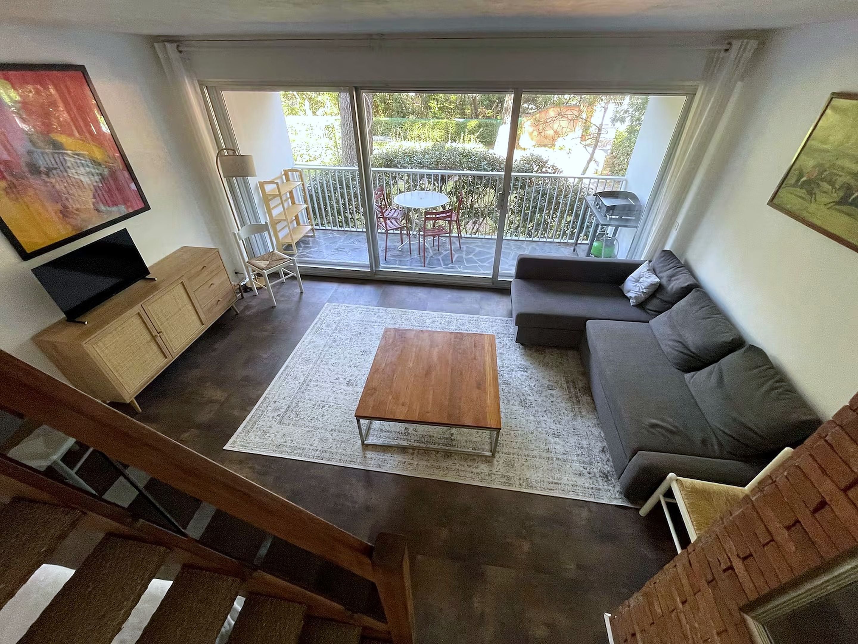 Een woonkamer met een bank, een salontafel, een televisie en een balkon met tuinmeubilair.