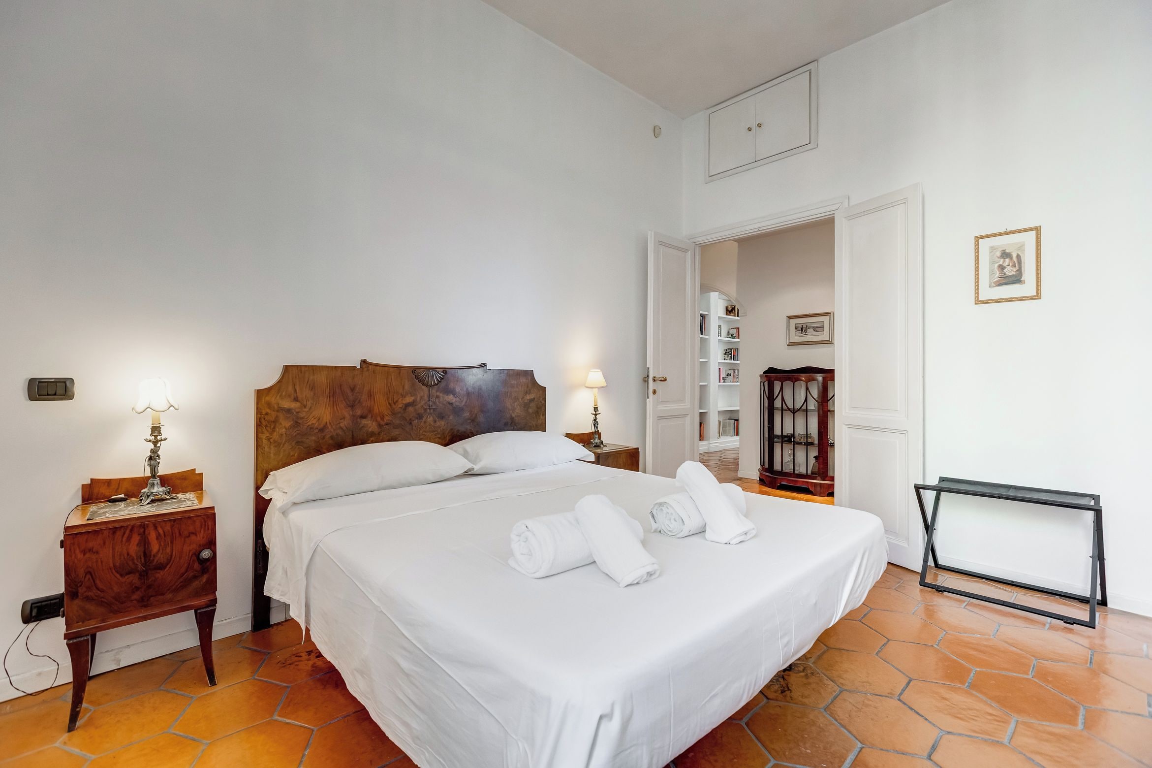 A hotel room with a large bed, a nightstand, a lamp, and a view of the hallway.