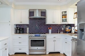 Una cocina moderna con armarios blancos, una campana extractora de acero inoxidable y un horno empotrado.