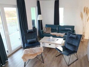 Ein modernes Wohnzimmer mit einer Couch, zwei Sesseln, einem Couchtisch und einer Stehlampe.