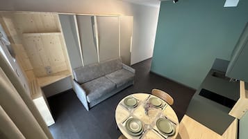 A compact living space with a sofa, a dining table set for four, and a kitchenette area.
