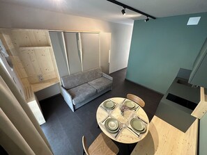 A compact living space with a sofa, a dining table set for four, and a kitchenette area. - Rifugio San Bernardo (Valdobbiadene)