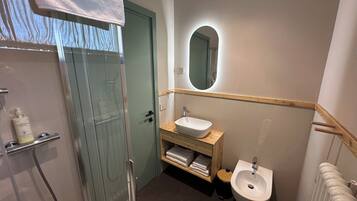 Ein modernes Badezimmer mit einer Duschkabine aus Glas, einem Holzbadezimmer-Möbelstück mit Waschbecken und Spiegel sowie einem Bidet.