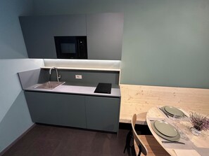 A compact kitchen with a built-in microwave, a sink, and a wooden dining table set with plates and cutlery. - Rifugio San Bernardo (Valdobbiadene)
