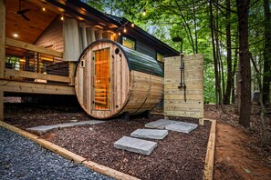 A wooden cabin with a large cylindrical structure, possibly a sauna, and a deck with a railing. - Sauna + Shower, Spa, Firepit, Gym, BBQ +EV Charger (Blue Ridge)