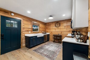 A compact kitchen with wooden walls, a dark blue door, and a white countertop. - Sauna + Shower, Spa, Firepit, Gym, BBQ +EV Charger (Blue Ridge)