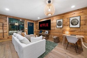 A modern living room with a white sofa, a television displaying 'NETFLIX', and wooden walls. - Sauna + Shower, Spa, Firepit, Gym, BBQ +EV Charger (Blue Ridge)