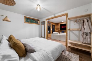 A bedroom with a bed, a wooden wardrobe, a hanging robe rack, and a TV displaying the Netflix logo. - Sauna + Shower, Spa, Firepit, Gym, BBQ +EV Charger (Blue Ridge)
