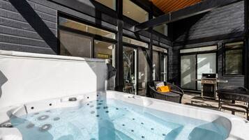Un bain à remous avec un plafond en bois et un barbecue à l’extérieur.