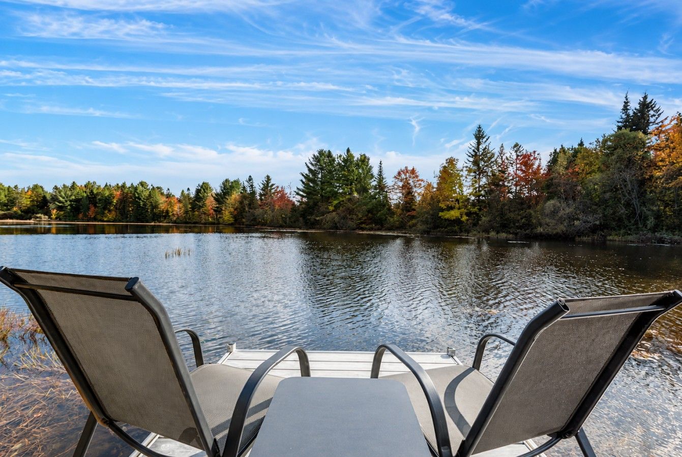 A boat with two chairs facing a calm lake surrounded by trees.