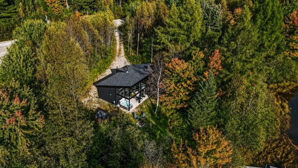Oversigtsbillede af et moderne hus omgivet af tæt skov, med en tydelig indkørsel til indgangen.