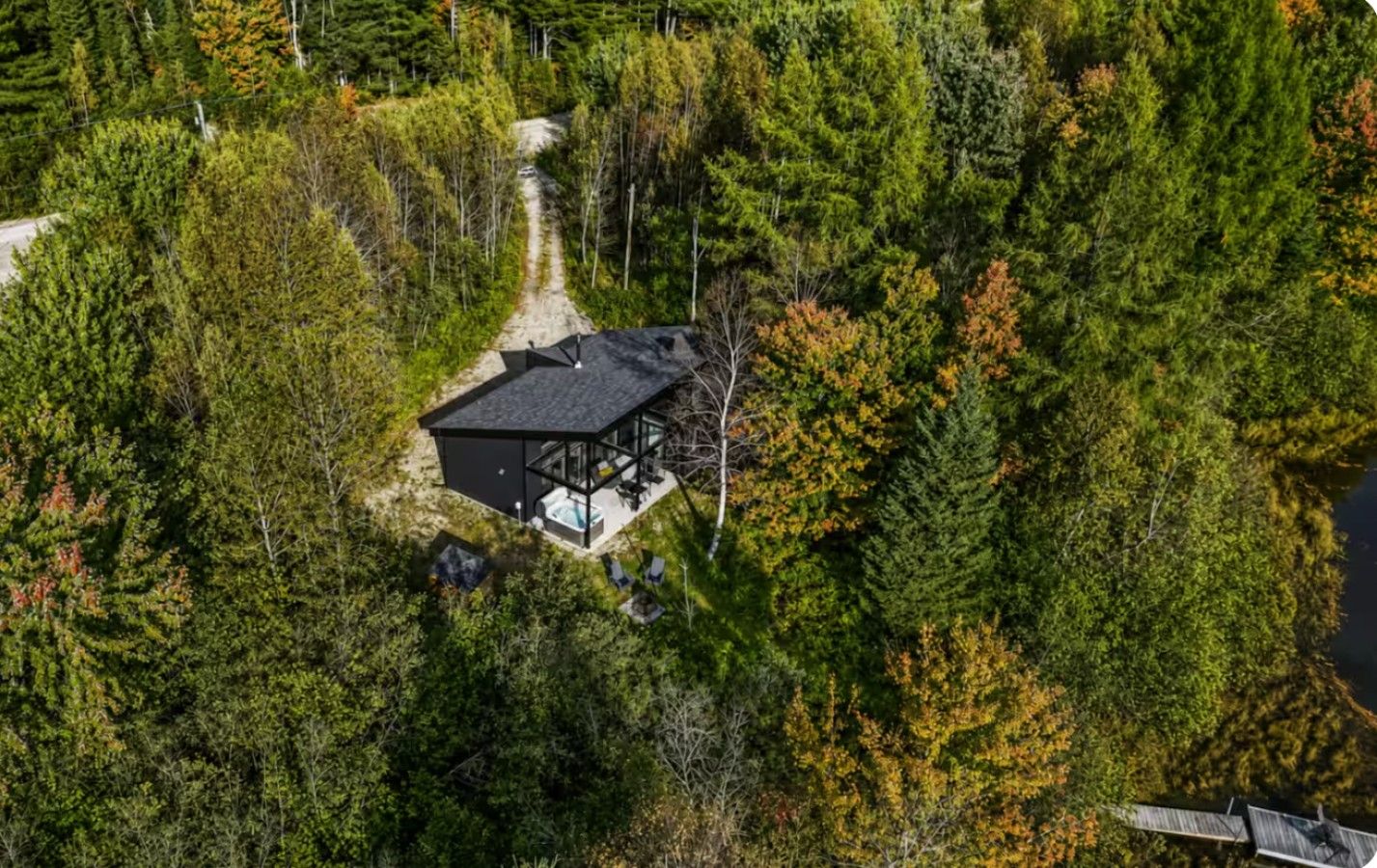 Un chalet isolé, doté d’une structure en verre, entouré d’une forêt dense et accessible par un sentier bien tracé.