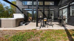 En moderne udendørs terrasse med et spabad, grill og havemøbler.