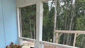 A wooden deck with a round table and two chairs, surrounded by potted plants.