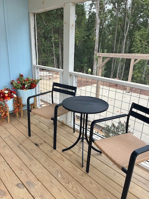 A wooden deck with a round table and two chairs, surrounded by potted plants.