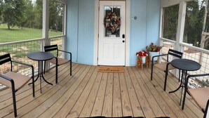A covered porch with two tables and chairs, a welcome mat, and a door with a wreath.