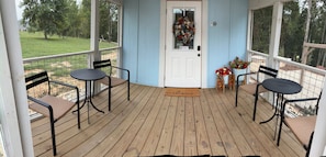 A covered porch with two tables and chairs, a welcome mat, and a door with a wreath.