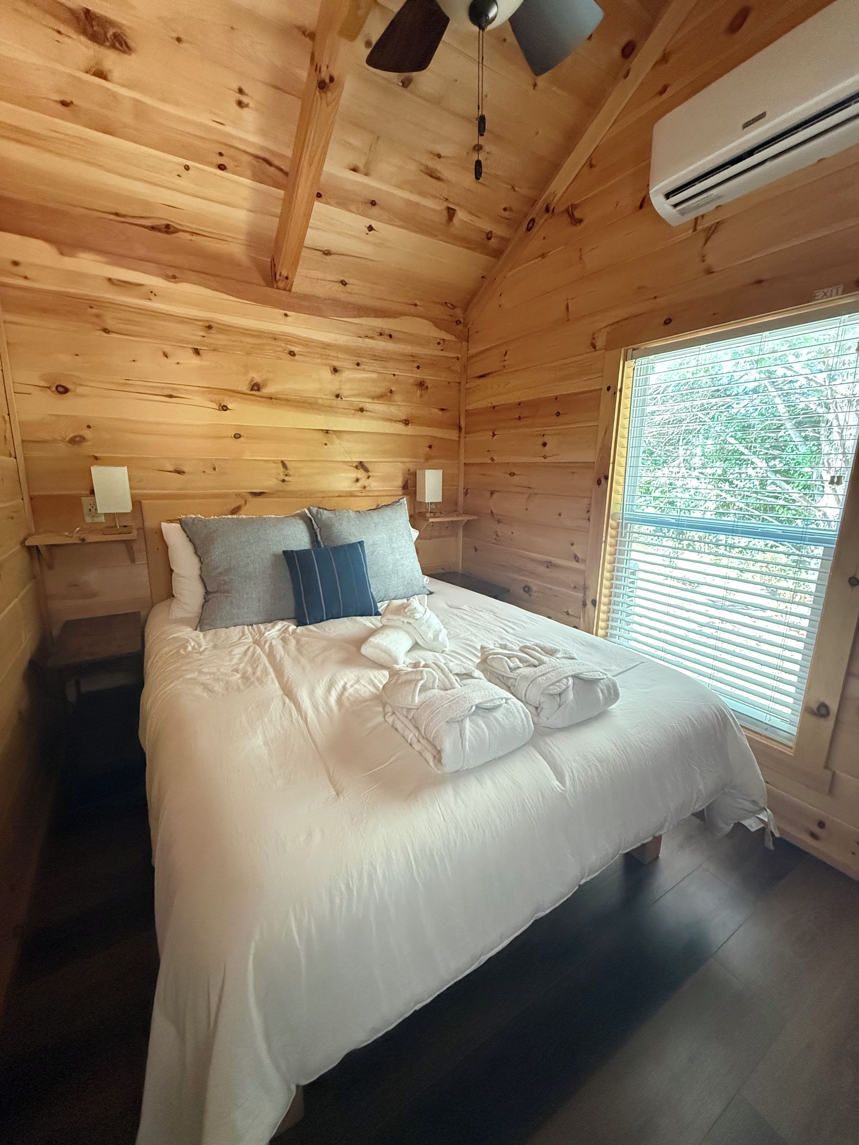Un dormitorio de cabaña de madera con cama, almohadas y un equipo de aire acondicionado.