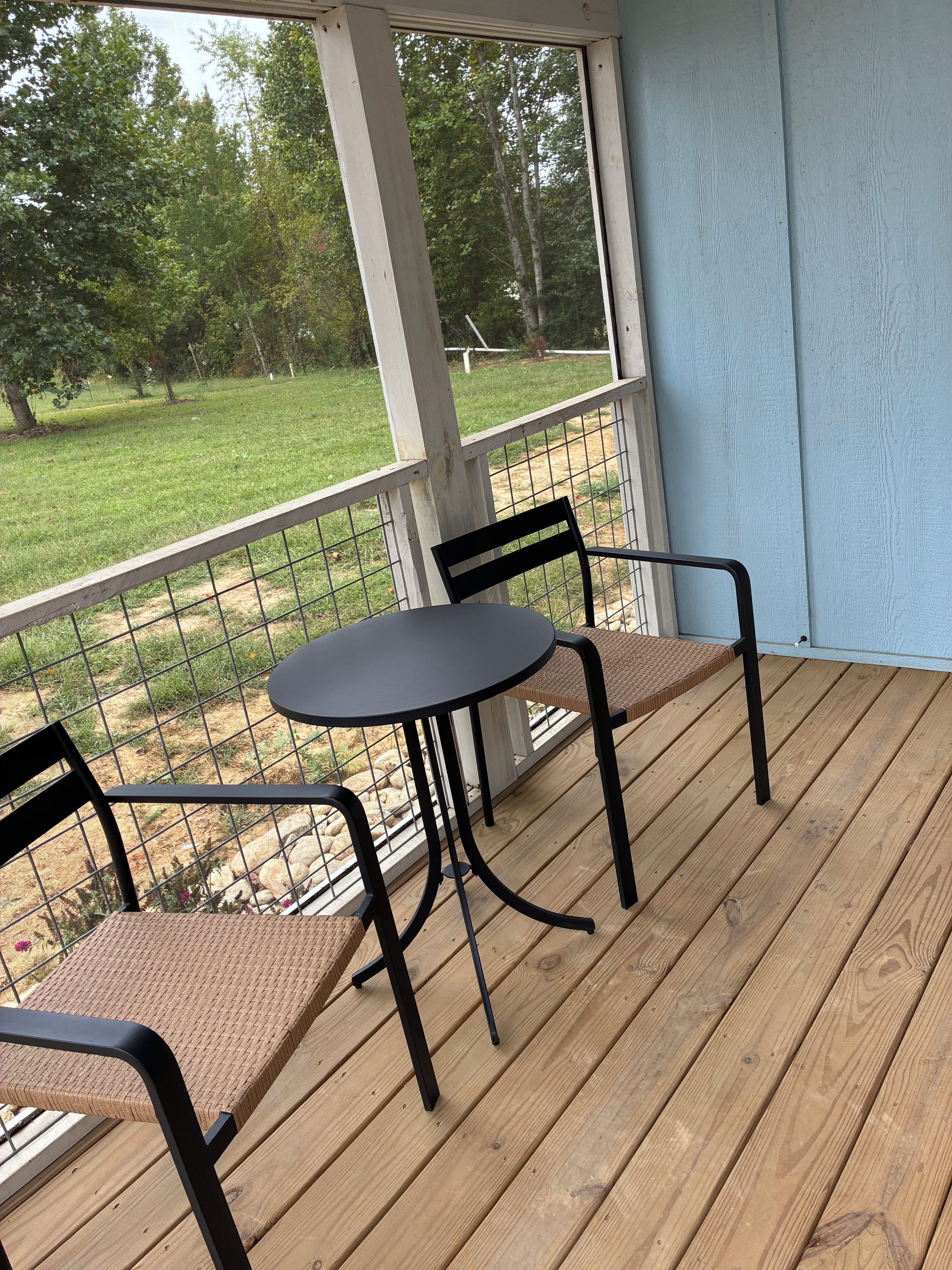 A covered outdoor area with a table and chairs, a view of a grassy yard, and a wooden deck.