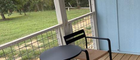 Ein überdachter Außenbereich mit Tisch und Stühlen, Blick auf eine Rasenfläche und eine Holzterrasse.