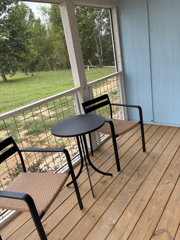 A covered outdoor area with a table and chairs, a view of a grassy yard, and a wooden deck.