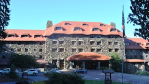 A large stone building with a red roof and multiple windows, surrounded by a well-maintained lawn and parked cars.