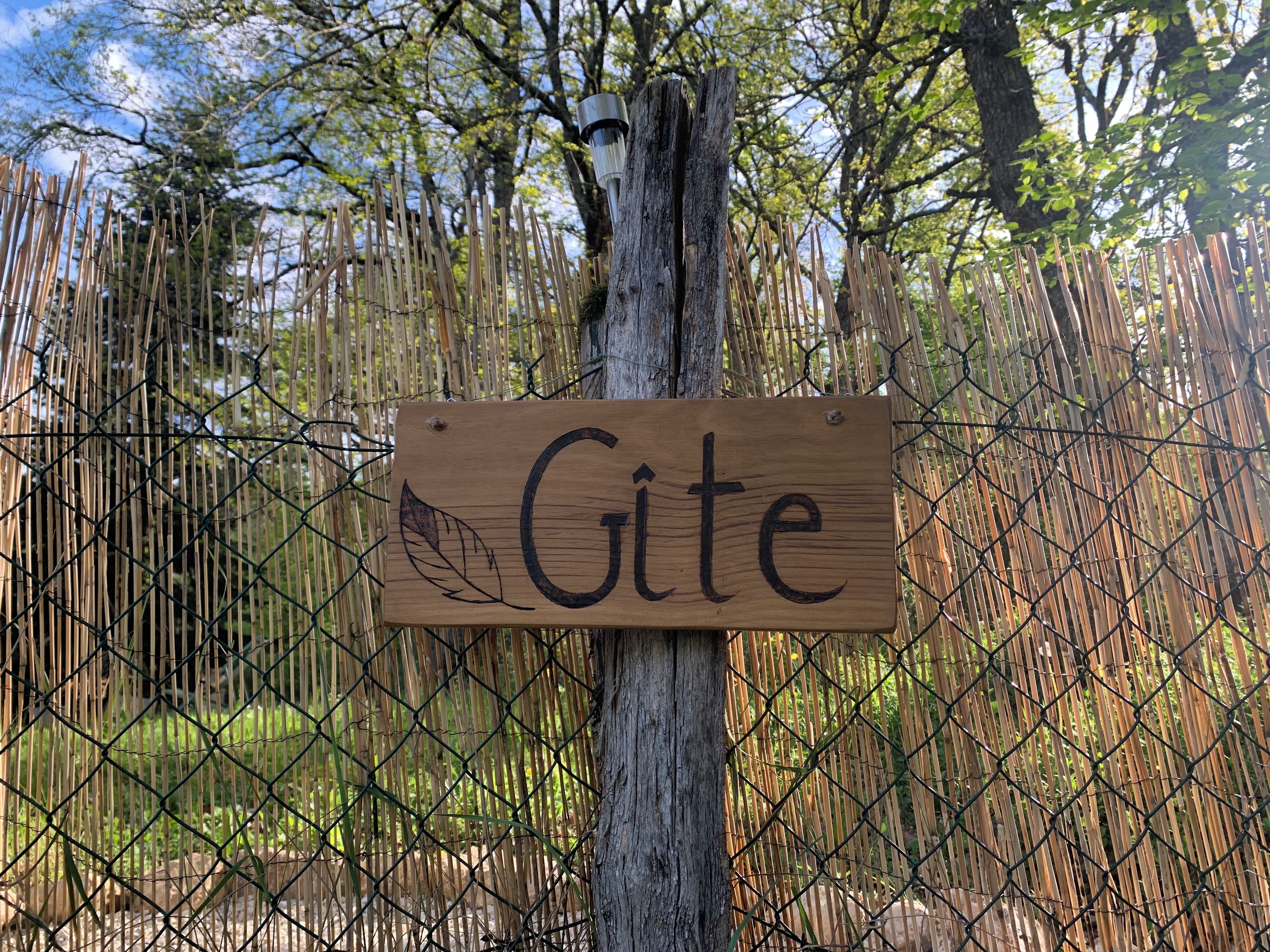 Ein Holzschild mit dem Wort 'Gite' an einem Baum befestigt, hinter einem Bambuszaun.