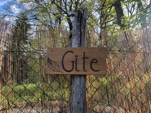 Ein Holzschild mit dem Wort 'Gite' an einem Baum befestigt, hinter einem Bambuszaun.