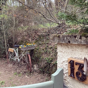 A rustic bicycle with a basket of flowers parked near a stone wall with a number plaque.