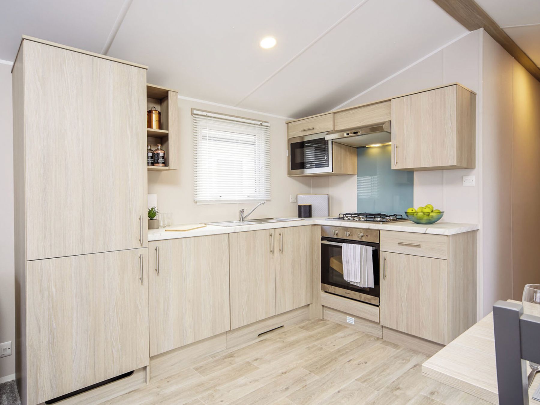 A compact kitchen with light wood cabinetry, a built-in microwave, a gas stove, and a small window.