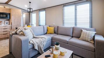 Een moderne woonkamer met een hoekbank, een salontafel en een keukenhoek met een magnetron.