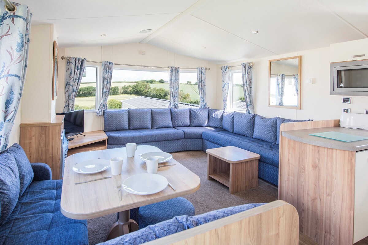 A modern RV interior with a sectional sofa, a dining table, and a kitchenette area.