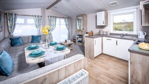 Et moderne campingvogns interiør med spiseplads, tekøkken og et stort vindue med udsigt over landskabet.