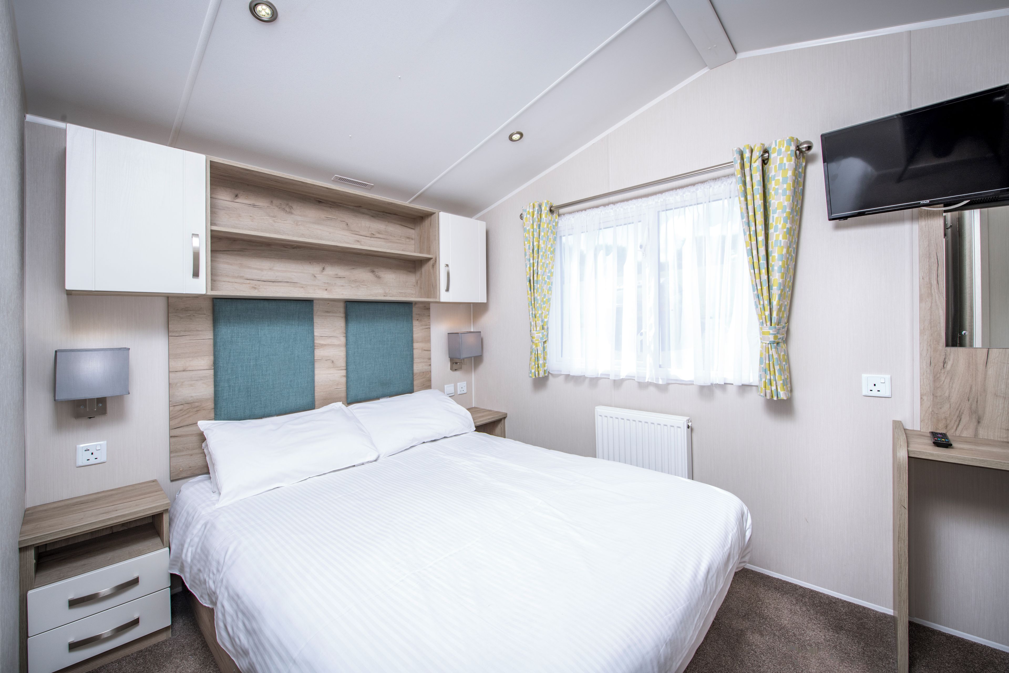 A hotel room with a bed, a TV, a desk, and a window with curtains.