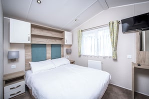 A hotel room with a bed, a TV, a desk, and a window with curtains. - Widemouth Bay Caravan Park (Near Bude)