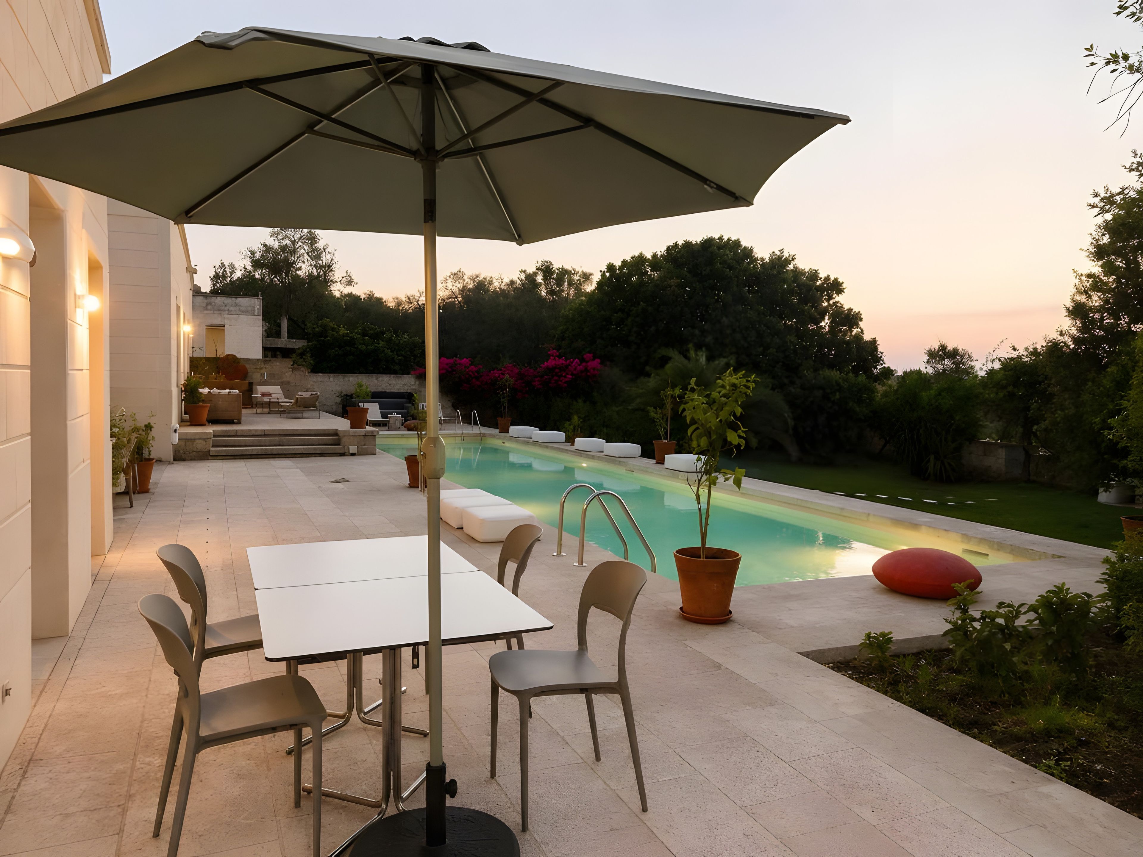 Ein Poolbereich mit Tisch und Stühlen, einem großen Sonnenschirm und einem Pool.