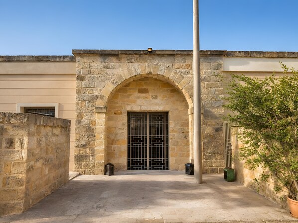 A stone building with an arched entrance, a flagpole, and a potted plant. - Villa “Masseria Baba” with Private Pool, Wi-Fi, and Air Conditioning (Nardò)