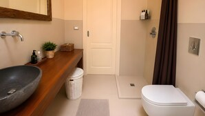 Een badkamer met een houten wastafelmeubel, een ruime wastafel, een toilet, een douche en een spiegel.
