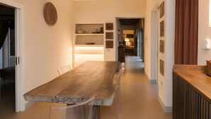 Een moderne keuken met een lange houten tafel, inbouwplanken en uitzicht op de eethoek.
