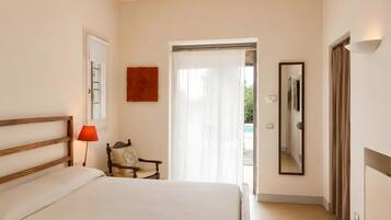 A hotel room with a bed, a chair, a lamp, a mirror, and a door leading to a balcony.