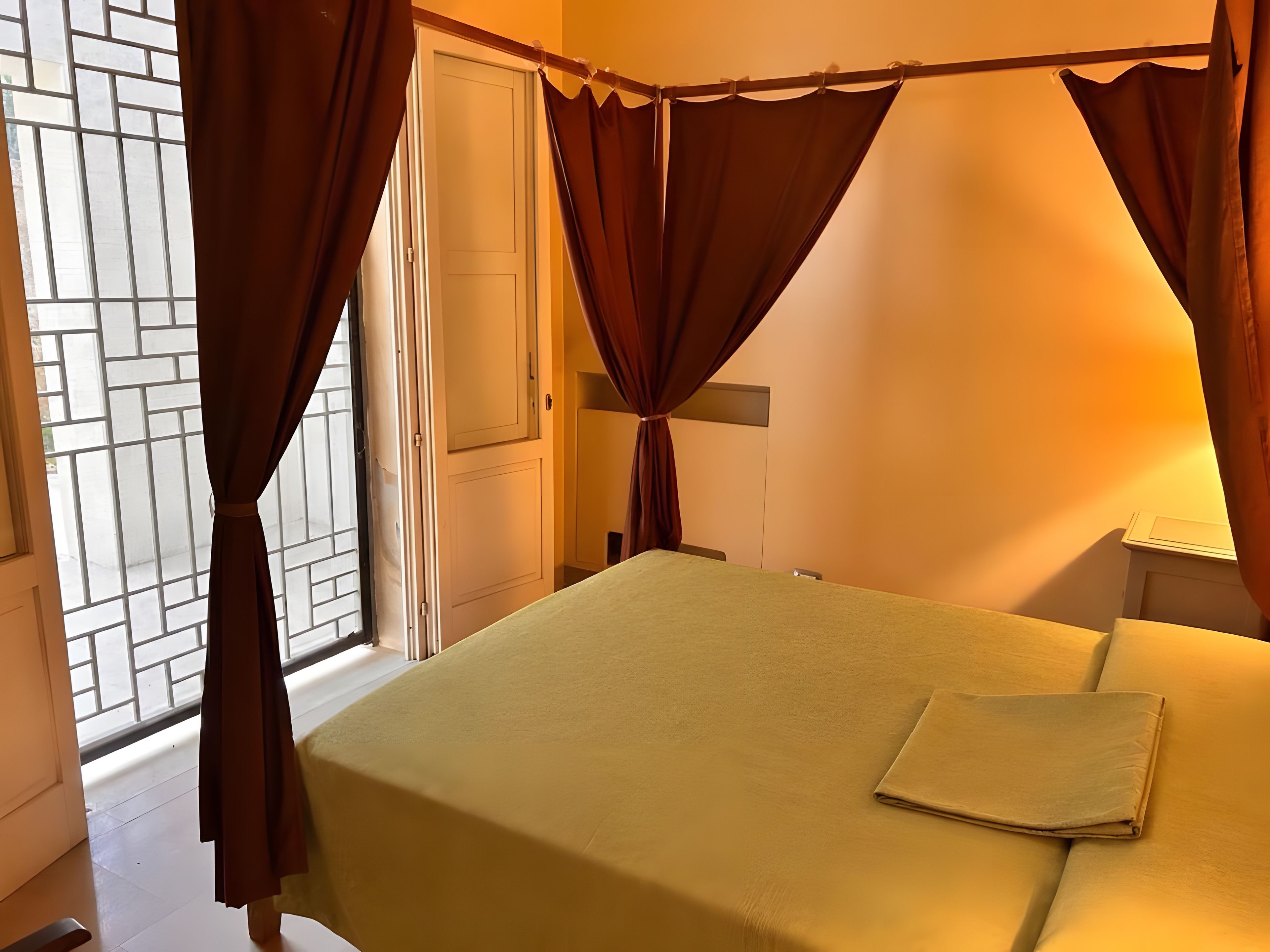 Ein Zimmer mit Bett, Vorhängen, einer Tür und einem Fenster.